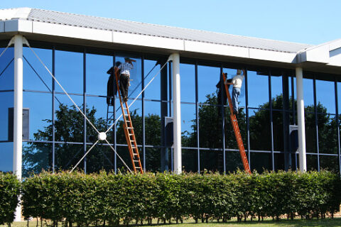 Commercial Building Window Cleaners Window cleaners on ladders cleaning exterior windows of a commercial office building